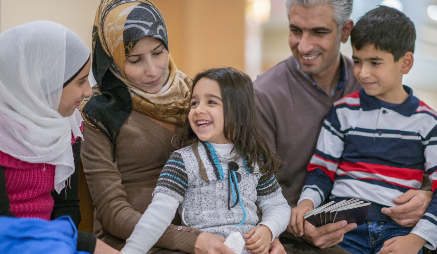 A Middle-eastern father, mother, brother and two sisters have just arrived to a new country. They are happily sitting together and smiling. The father is holding his family's passports. Their luggage is sitting to the side © FatCamera