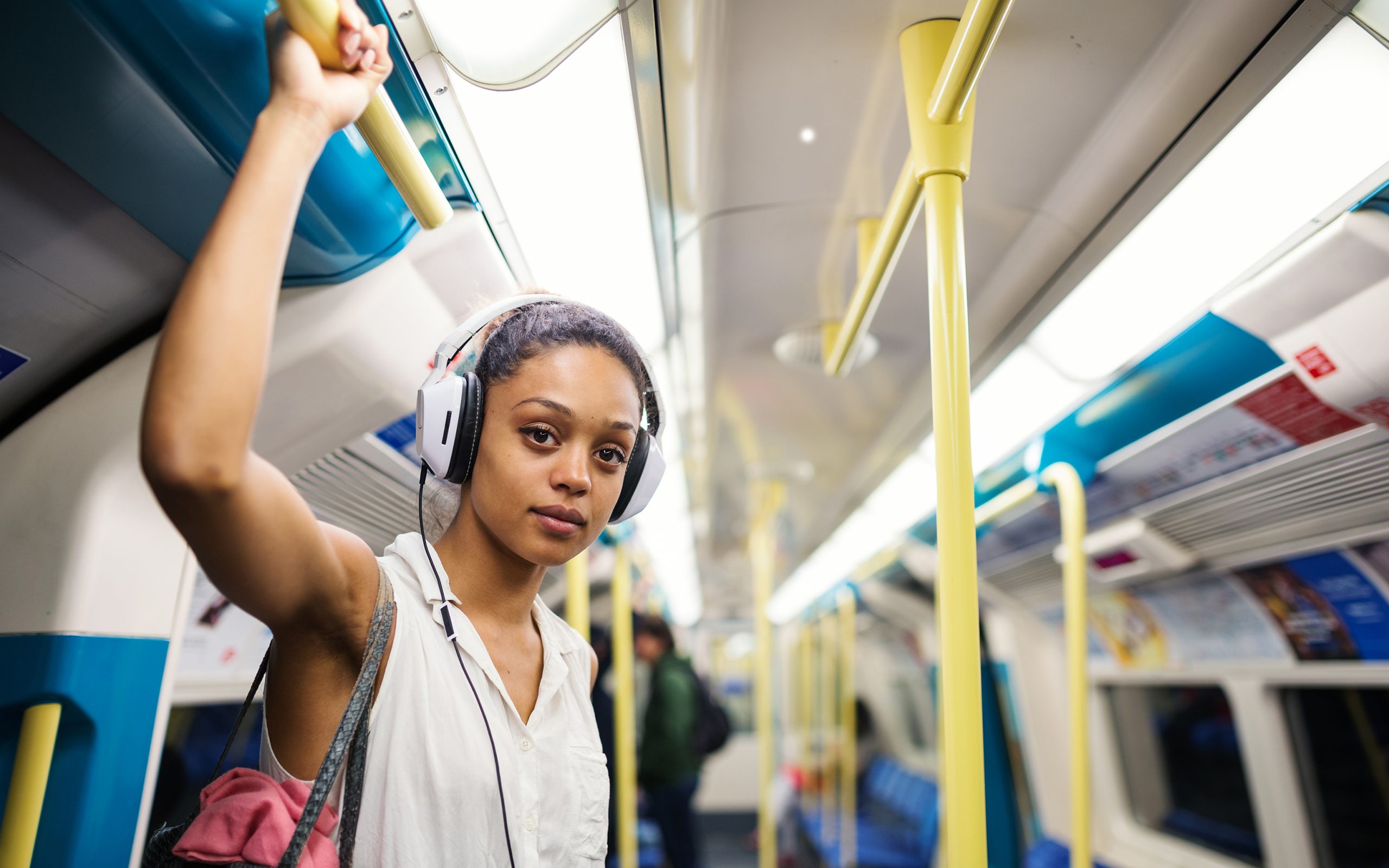 Young person in their early twenties standing up on a tube train wearing headphones